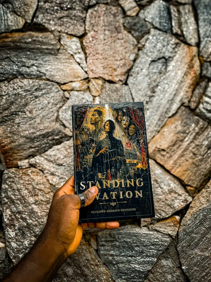 The author holding the printed hardcopy of Standing Ovation against a stone wall